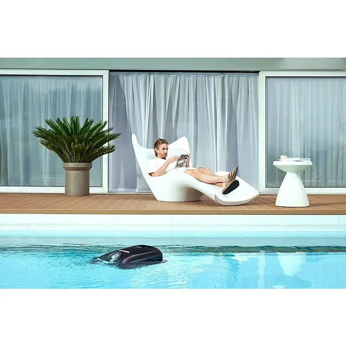 Beatbot Poolroboter AquaSense 2 Pro - Akkubetrieben, Passend für: Pools bis 360 m² Grundfläche, Filterleistung: 20.800 l/h - Bild eines automatischen Poolreinigers im Einsatz, während sich eine Person am Pool entspannt und liest. Der Reiniger sorgt für Sauberkeit.