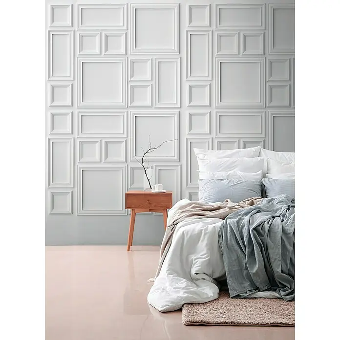 A.S. Création The Wall 3 Fototapete Bilderrahmen - B x H: 159 x 280 cm, Vlies - Ein Schlafzimmer mit einem stilvollen Holznachttisch und einer kunstvollen weißen Wanddekoration über dem Bett.