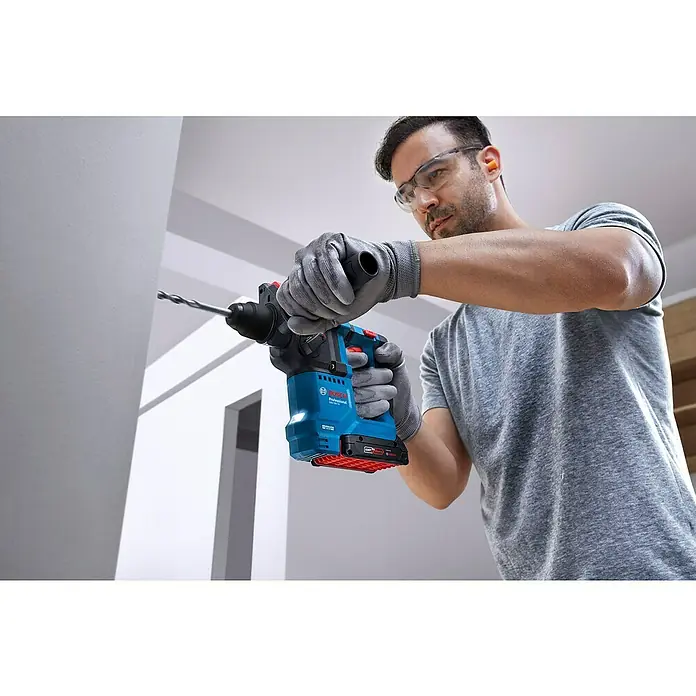Bosch Professional AMPShare 18V Akku-Bohrhammer GBH 18V-18 - 18 V, Ohne Akku, 1,5 J - Ein Mann bohrt mit einer blauen Bosch Professional Akku-Bohrmaschine ein Loch in eine weiße Wand. Er trägt Schutzbrille und Handschuhe.