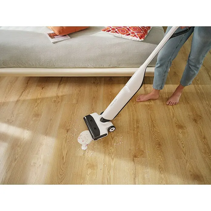 Roborock Akku-Nass-Trockensauger Flexi Lite - Saugkraft: 17.000 Pa, Akkulaufzeit: 40 min, Wassertankvolumen: 0,62 l - Das Bild zeigt einen Roborock Staubsauger, der Flüssigkeiten auf einem Holzboden aufsaugt. Eine Person steht barfuß daneben.