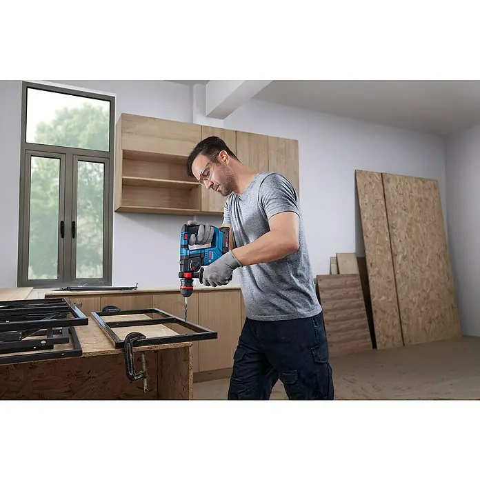 Bosch Professional AMPShare 18V Akku-Bohrhammer GBH 18V-18X - 18 V, Ohne Akku, 1,5 J - Ein Mann bohrt mit einer blauen Bosch-Bohrmaschine durch ein Metallstück. Die Bohrmaschine ist kabellos und leistungsstark.