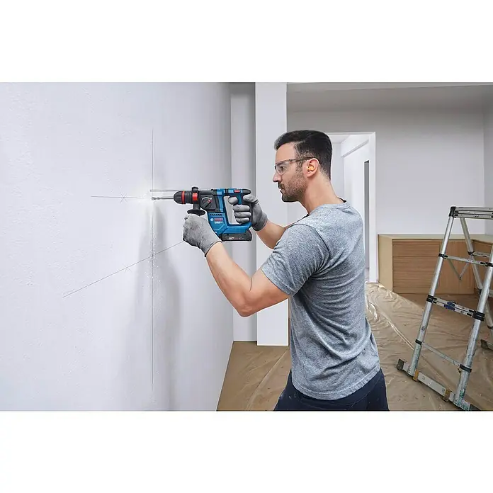 Bosch Professional AMPShare 18V Akku-Bohrhammer GBH 18V-18X - 18 V, Ohne Akku, 1,5 J - Ein Handwerker bohrt mit einer blauen Bosch-Bohrmaschine ein Loch in eine Wand, um etwas zu befestigen. Er trägt Schutzbrille und Handschuhe.