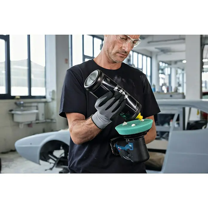Bosch Professional Akku-Poliermaschine GPX 12V-125 - 12 V, Ohne Akku, Leerlaufdrehzahl: 1.400 U/min - 7.000 U/min - Ein Mann trägt Polierpaste auf ein Akku-Poliergerät auf. Das Gerät hat einen grünen Polierschwamm. Der Mann trägt eine Schutzbrille und Handschuhe.