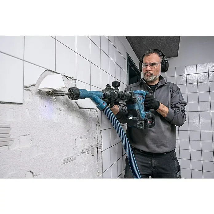 Bosch Professional AMPShare 18V Akku-Schlaghammer GSH 18V-5 - 18 V, Ohne Akku, 8,5 J - Ein Handwerker demontiert mit einem Bosch Abbruchhammer Fliesen von einer Wand, während er Schutzbrille und Kopfhörer trägt.