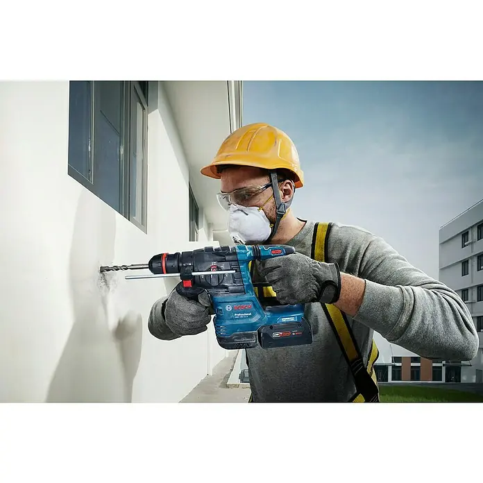 Bosch Professional AMPShare 18V Akku-Bohrhammer GBH 18V-22X - 18 V, Ohne Akku, 2 J - Ein Bauarbeiter bohrt mit einer Bosch Professional Akku-Bohrmaschine ein Loch in eine Wand. Die Bohrmaschine ist blau und schwarz.
