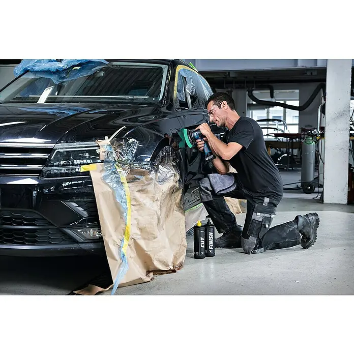 Bosch Professional Akku-Poliermaschine GPX 12V-125 - 12 V, Ohne Akku, Leerlaufdrehzahl: 1.400 U/min - 7.000 U/min - Ein Mann poliert mit einer Poliermaschine die Karosserie eines schwarzen Autos in einer Werkstatt. Auf dem Boden stehen zwei Flaschen mit Polierflüssigkeit.