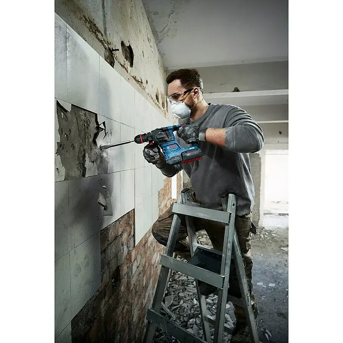 Bosch Professional AMPShare 18V Akku-Bohrhammer GBH 18V-22X - 18 V, Ohne Akku, 2 J - Ein Handwerker benutzt einen Bosch-Bohrhammer, um Fliesen von einer Wand zu entfernen, während er auf einer Leiter steht.