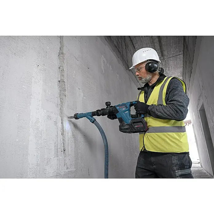 Bosch Professional AMPShare 18V Akku-Schlaghammer GSH 18V-5 - 18 V, Ohne Akku, 8,5 J - Ein Bauarbeiter verwendet einen Bosch Abbruchhammer mit Staubabsaugung, um eine Wand zu bearbeiten. Er trägt Schutzkleidung für seine Sicherheit.