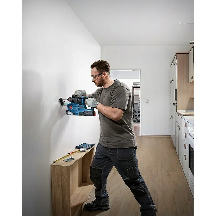 Bosch Professional AMPShare 18V Akku-Bohrhammer GBH 18V-22X - 18 V, Ohne Akku, 2 J - Handwerker bohrt mit einer Bosch-Bohrmaschine in eine Wand, um ein Regal zu befestigen. Schutzbrille und Handschuhe werden getragen.