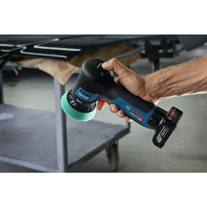 Bosch Professional Akku-Poliermaschine GPO 12V-77 - 12 V, Ohne Akku, Leerlaufdrehzahl: 600 U/min - 2.200 U/min - Nahaufnahme eines Bosch Akku-Polierers mit Schleifscheibe, der von einer Hand bedient wird, vor einer Werkstattkulisse.