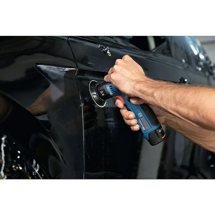 Bosch Professional Akku-Exzenterschleifer GEX 12V-77 - 12 V, Ohne Akku, Durchmesser Schleifteller: 77 mm - Detailaufnahme eines Bosch Professional Akku-Polierers, der an einem schwarzen Auto verwendet wird. Das Werkzeug ist blau und schwarz.