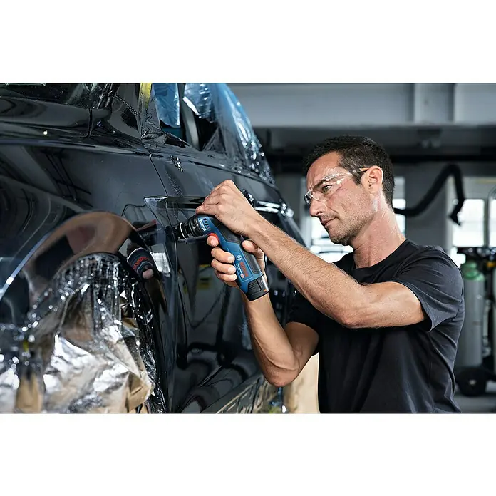 Bosch Professional Akku-Schwingschleifer GSS 12V-32 - 12 V, Ohne Akku, Leerlaufschwingzahl: 6.000 U/min - 16.000 U/min - Ein Handwerker verwendet einen Bosch GOP 12V-28 Multifunktionsschneider an einem schwarzen Auto, um präzise Anpassungen vorzunehmen. Die Werkzeuge sind für Profis.