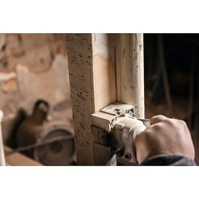 Scheppach Lijadora excéntrica eléctrica LFR720 - 720 W - Un artesano utiliza un cepillo para refinar el borde de un marco de madera, eliminando virutas. La herramienta está situada centralmente en la imagen.