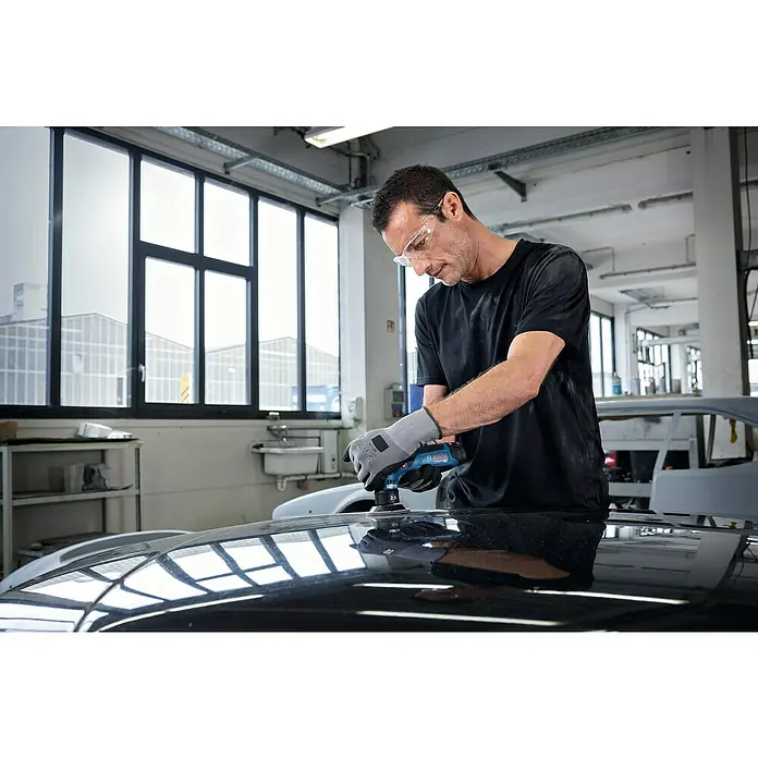 Bosch Professional Akku-Exzenterschleifer GEX 12V-77 - 12 V, Ohne Akku, Durchmesser Schleifteller: 77 mm - Ein Mann poliert mit einer blauen Bosch Poliermaschine die Motorhaube eines schwarzen Autos in einer Werkstatt.