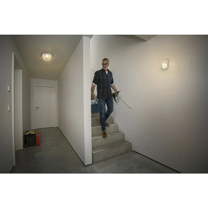 Osram Wand- & Deckenleuchte Bulkhead Essential - L x B x H: 9,8 x 11 x 20,7 cm, Weiß, E27 - Mann geht Treppe runter, beleuchtet von einer Deckenleuchte und einer Wandleuchte, mit Werkzeugkasten und Bohrmaschine.