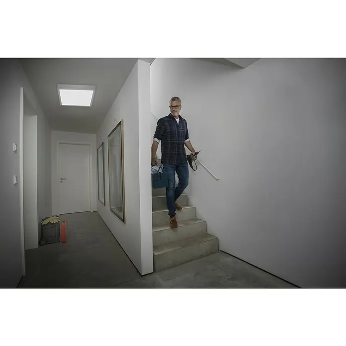 Ledvance LED-Panel Frame Essential - Weiß, Passend für: Osram Essential LED-Panel 60 x 60 cm - Ein Mann geht die Treppe hinunter und hält eine Werkzeugkiste und einen Bohrer in der Hand. Helle, moderne Innenraumbeleuchtung.