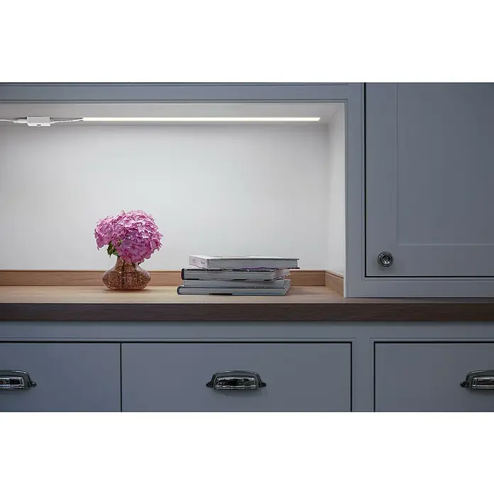 Osram LED-Feuchtraumlichtleiste - Kaltweiß, Länge: 127,7 cm, IP65, 16 W, 1.300 lm - Nahaufnahme eines Unterschranks mit Arbeitsplatte, auf der ein Licht unter dem Schrank, eine Vase mit Blumen und einige Bücher stehen.