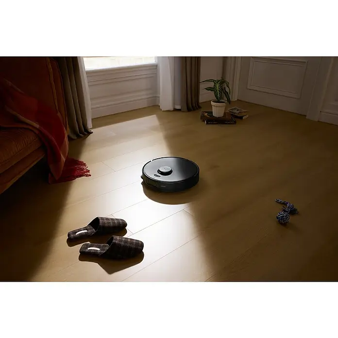 Roborock Saugwischroboter Qrevo Edge 5V1 Black - Saugkraft: 18.500 Pa, Akkulaufzeit: 180 min, Fassungsvermögen Roboter: 325 ml, Schwarz - Ein schwarzer Roboterstaubsauger steht auf einem Holzboden neben Hausschuhen und einem Spielzeug. Er sorgt für Sauberkeit im Haus.