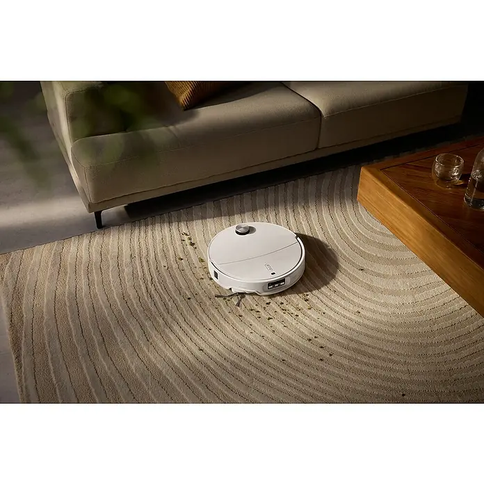 Roborock Saugwischroboter Qrevo CurvX White - Saugkraft: 22.000 Pa, Akkulaufzeit: 220 min, Fassungsvermögen Roboter: 330 ml - Ein weißer Saugroboter reinigt einen Teppich in einem Wohnzimmer, während er unter einem Sofa und neben einem Couchtisch steht.