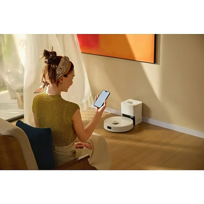 Roborock Saugwischroboter Q10 VF+ White - Saugkraft: 10.000 Pa, Akkulaufzeit: 240 min, Fassungsvermögen Roboter: 350 ml, Weiß - Frau, die einen Roboterstaubsauger mit ihrem Smartphone steuert. Das moderne Gerät erleichtert die Hausarbeit im smarten Zuhause.
