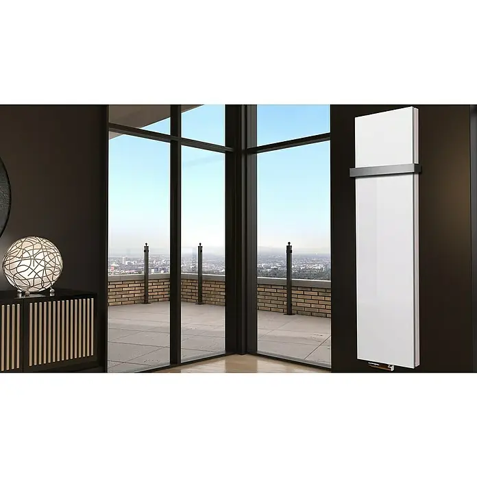 Badheizkörper Manhattan - B x H: 470 x 1.800 mm, Weiß, 1 x Halter 50mm, Nennleistung: 1.964 W - Ein moderner, weißer Heizkörper hängt an einer dunklen Wand. Im Hintergrund eine Fensterfront mit Ausblick auf eine Stadt.
