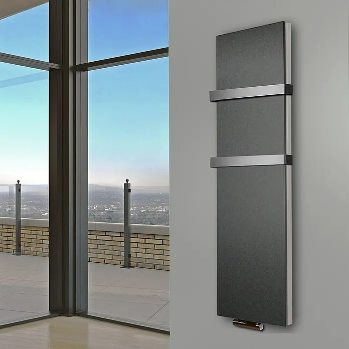 Badheizkörper Manhattan - B x H: 470 x 1.800 mm, Moonstone, 2 x Halter 50mm, Nennleistung: 1.964 W - Ein moderner, grauer Heizkörper mit horizontalen Chromakzenten hängt an einer grauen Wand. Im Hintergrund ist ein Fenster mit Ausblick.