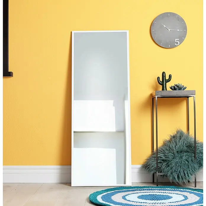 Espejo de pared Tampere - 43 x 133 cm, Blanco - Un espejo delgado con marco blanco se apoya contra una pared amarilla, complementado con elementos decorativos para un aspecto moderno.
