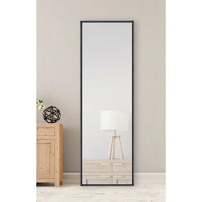Espejo de pared Tampere - 43 x 133 cm, Negro - Un espejo rectangular y elegante con un marco delgado y oscuro se sitúa junto a una cómoda, reflejando una lámpara.
