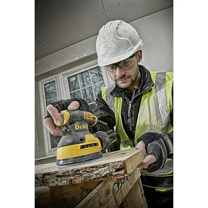 DeWalt Elektro-Exzenterschleifer DWE6423 - 280 W, Durchmesser Schleifteller: 125 mm - Ein Bauarbeiter verwendet einen DeWalt Exzenterschleifer, um ein Holzbrett zu schleifen, während er Schutzkleidung trägt.