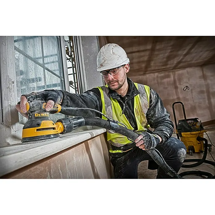 DeWalt Elektro-Exzenterschleifer DWE6423 - 280 W, Durchmesser Schleifteller: 125 mm - Ein Handwerker benutzt einen DeWalt Exzenterschleifer, um eine Fensterbank zu bearbeiten. Der Schleifer ist gelb und schwarz und hat einen Staubsaugeranschluss.