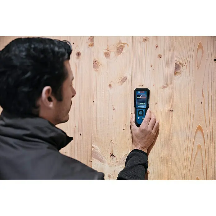Bosch Feuchtigkeitsmessgerät GMM 1-15 - Messgenauigkeit: ± 0,4 mm/m, Mit Batterien - Ein Mann prüft mit einem Bosch Feuchtigkeitsmessgerät GMS 100 M Professional den Feuchtigkeitsgehalt einer Holzwand, um die Trockenheit zu beurteilen.
