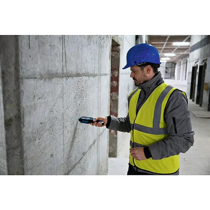 Bosch Feuchtigkeitsmessgerät GMP 1-13 - Messgenauigkeit: Umgebungstemperatur typisch: +/- 1 °C, Mit Batterien - Ein Bauarbeiter mit Schutzhelm und Warnweste prüft eine Betonwand mit einem Bosch Ortungsgerät.