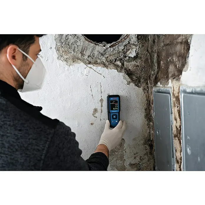Bosch Feuchtigkeitsmessgerät GMM 1-15 - Messgenauigkeit: ± 0,4 mm/m, Mit Batterien - Mann mit Feuchtigkeitsmesser von Bosch Professional zur Messung des Feuchtigkeitsgehalts in einer Wand.