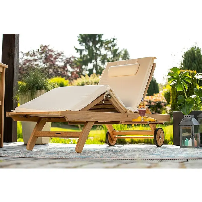 Kai Wiechmann Gartenliege - Naturbelassen, Holz, Rollbar - Ein hölzerner Liegestuhl mit cremefarbener Polsterung steht im Freien, ideal zum Entspannen und Genießen des Gartens bei schönem Wetter.