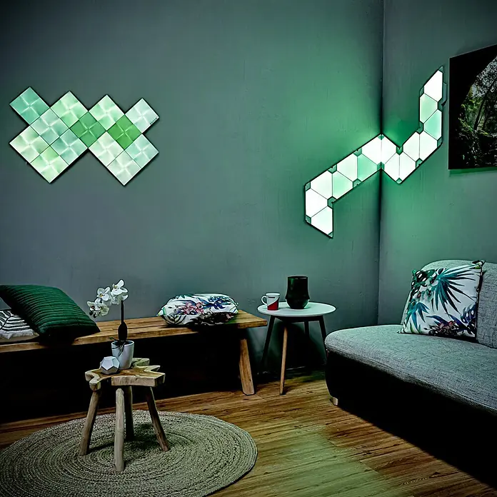 Nanoleaf Erweiterungskit Canvas 4 Panels - 4 Stk., 4 W, Weiß, RGBW, Canvas, Smart Home-fähig: Ja - Nanoleaf Light Panels in einem gemütlichen Wohnzimmer, die grüne Farbakzente setzen. Die Panels sind dekorativ an der Wand angebracht.