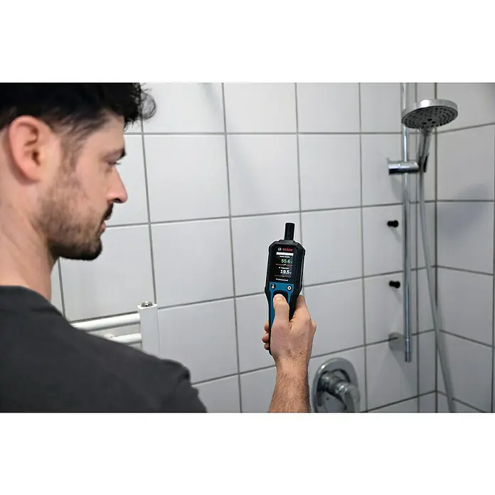 Bosch Thermo-Hygrometer GDH 1-17 - Mit Batterien - Ein Mann prüft die Luftfeuchtigkeit im Badezimmer mit einem Bosch Feuchtigkeitsmessgerät. Das Gerät zeigt 55,6 % relative Luftfeuchtigkeit und 19,5 °C Temperatur an.
