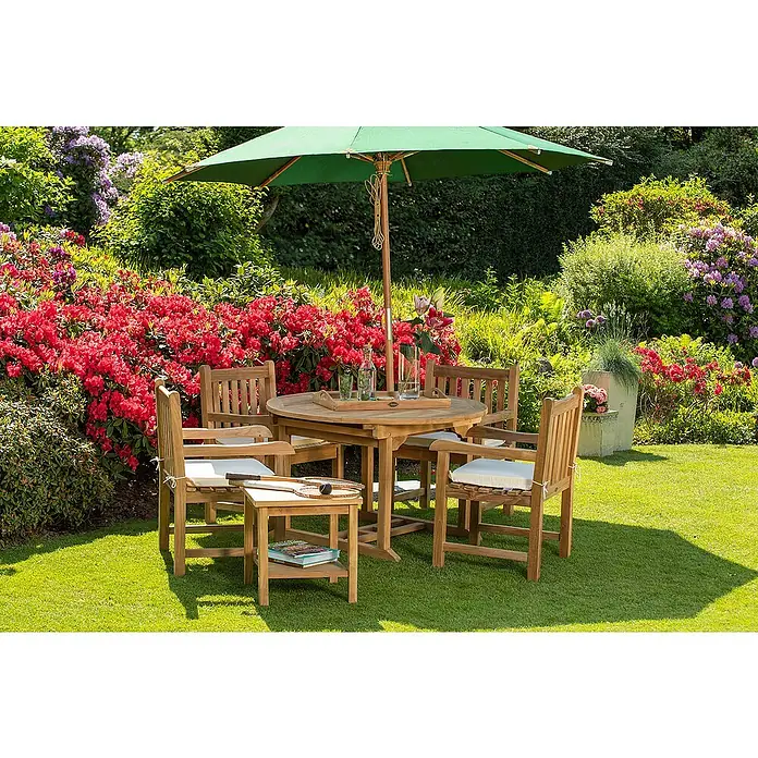 Kai Wiechmann Garten-Beistelltisch - Teakholz, Quadratisch, Naturbelassen - Ein Gartentischset aus Holz mit vier Stühlen und einem Sonnenschirm, umgeben von blühenden Büschen und Grün, lädt zum Verweilen ein.