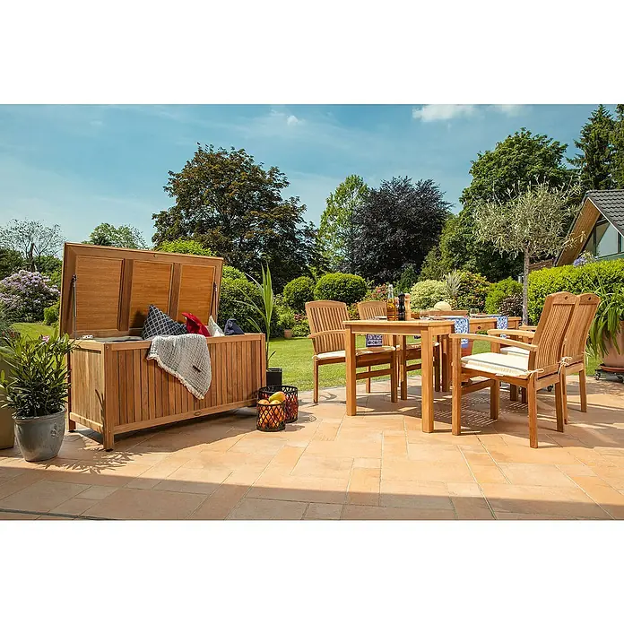 Kai Wiechmann Gartensessel - Teakholz, Stapelbar, Naturbelassen, B x T x H: 63 x 65 x 94 cm - Holzkiste und Gartenmöbel auf der Terrasse. Die Holzkiste ist geöffnet und mit Kissen und einer Decke gefüllt.