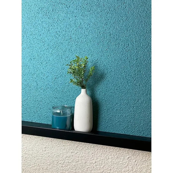 Floxxan Baumwollputz Colorado 154 - Putz Tapete Flüssigtapete Seegras - Seegras, 1 kg, Lösemittelfrei - Dekorative Szene mit einer blauen Kerze, einer weißen Vase mit Grünpflanzen, die auf einem eleganten schwarzen Regal vor einer strukturierten Wand stehen.