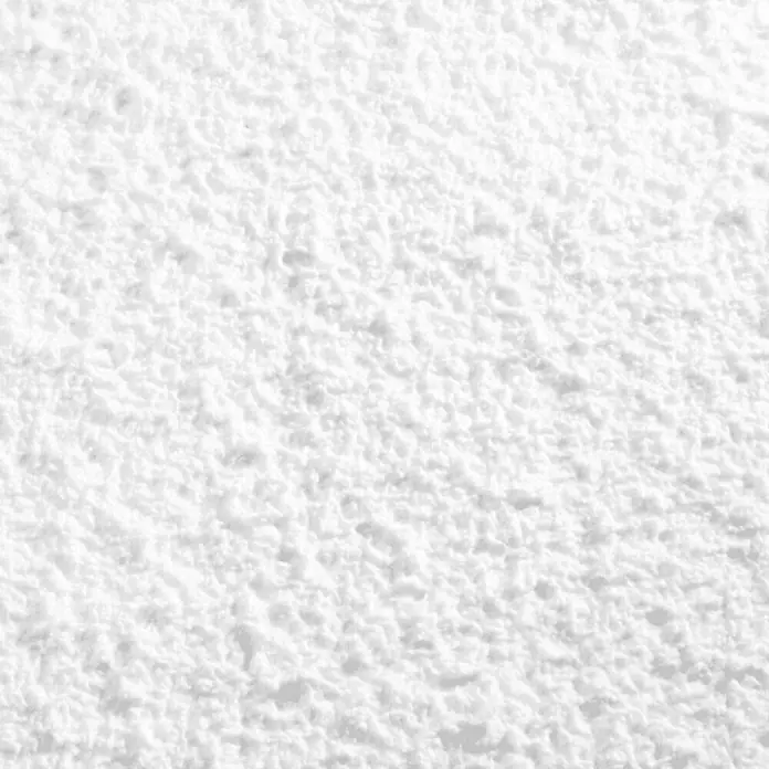 Floxxan Baumwollputz Colorado 101 - Putz Tapete Flüssigtapete Weiß - Weiß, 1 kg, Lösemittelfrei - Nahaufnahme einer weißen, strukturierten Oberfläche, die an Rauputz erinnert. Das Licht betont die unebene Textur.