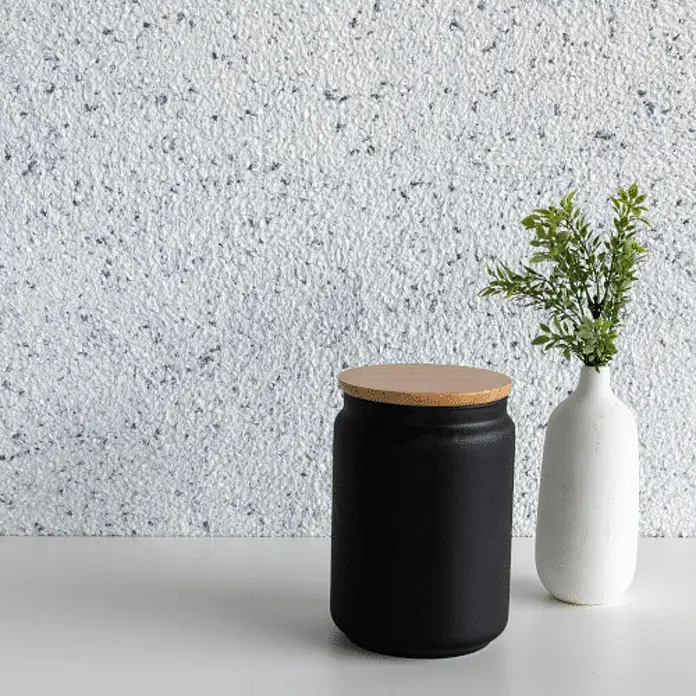 Floxxan Baumwollputz Montana 503 Cellulose - Putz Tapete Flüssigtapete Anthrazit - Anthrazit, 1 kg, Lösemittelfrei - Produktfoto: Ein schwarzer Vorratsbehälter mit Holzdeckel steht neben einer weißen Vase mit grünen Zweigen auf einem weißen Tisch.