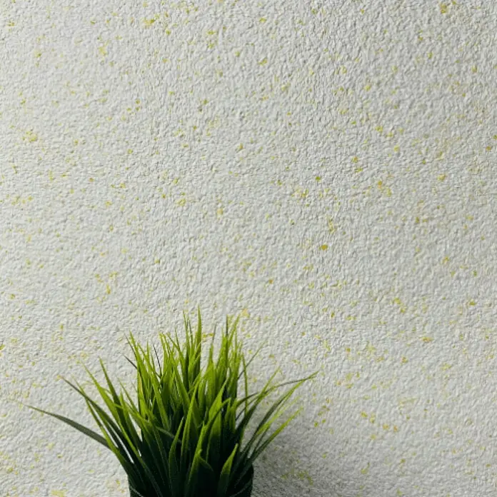 Floxxan Baumwollputz Montana 514 Cellulose - Putz Tapete Flüssigtapete Yellow - Yellow, 1 kg, Lösemittelfrei - Detailaufnahme einer Zimmerpflanze im Topf vor einer strukturierten, hellen Wand mit gelben Sprenkeln.