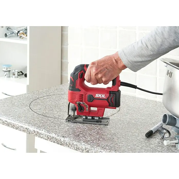Skil Elektro-Pendelhubstichsäge 4530 AA - 0 /min - 3.000 /min, Max. Schnitttiefe in Holz: 75 mm, Anzahl Pendelhubstufen: 4 Stk. - Rote SKIL Stichsäge schneidet ein Loch in eine Arbeitsplatte, während ein Handwerker sie bedient.