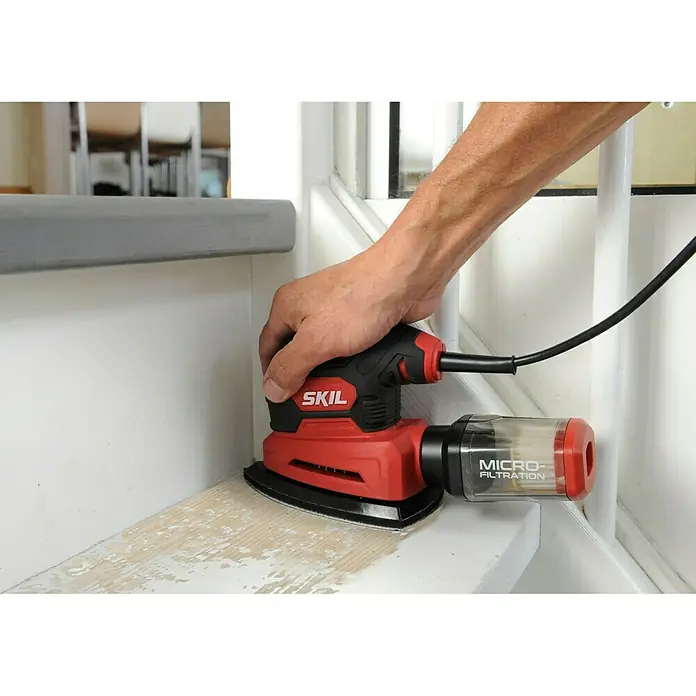 Skil Elektro-Multischleifer 7260 AA - 100 W, Leerlaufschwingzahl: 24.000 U/min, Durchmesser Schwingkreis: 1,6 mm - Nahaufnahme eines roten SKIL-Elektroschleifers mit Staubabsaugung beim Schleifen einer Treppenstufe.