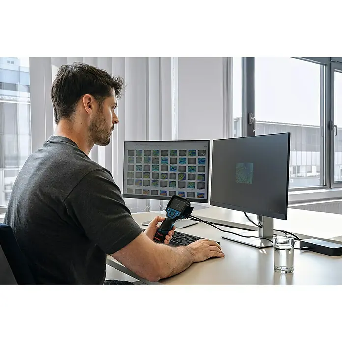 Bosch Professional Wärmebildkamera GTC 12V-450-13 Solo - -20 °C - 450 °C - Ein Mann betrachtet Wärmebilder auf zwei Monitoren, während er ein Bosch-Wärmebildgerät in der Hand hält, um Temperaturen zu analysieren.