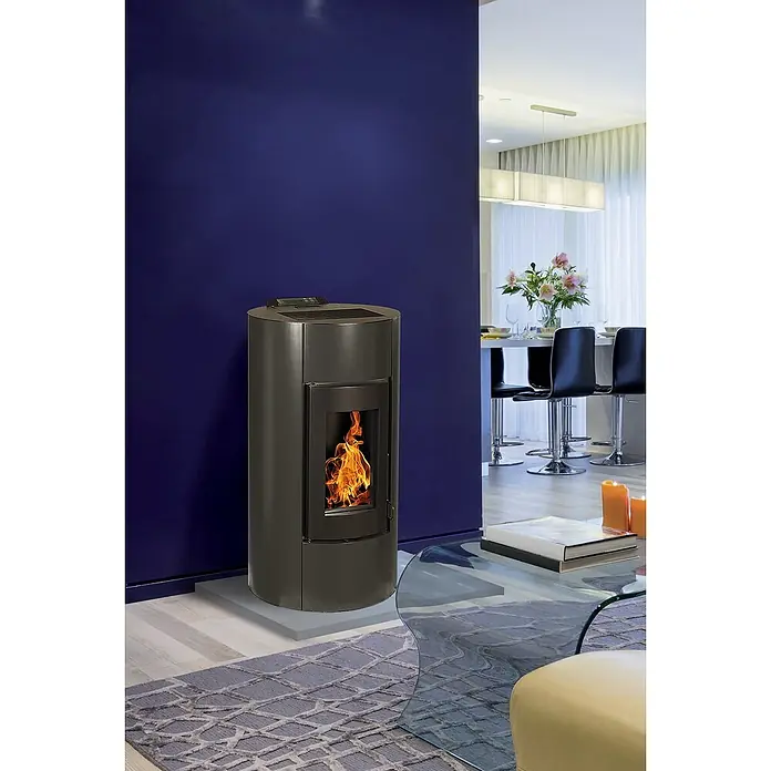 Pelletofen Angelina - 8,9 kW, Raumheizvermögen: 250 m³, 0,73 kg/h - 1,96 kg/h, Farbe Verkleidung: Schwarz - Ein Pelletofen mit Flammen steht in einem modernen Wohnzimmer mit blauer Wand und Glas Couchtisch.