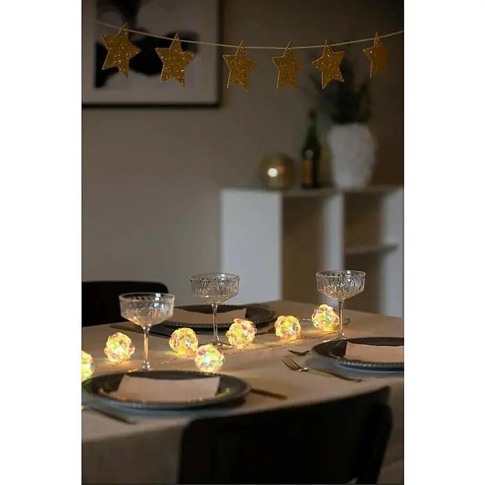 Konstsmide LED-Lichterkette - Innen, Lichtfarbe: Warmweiß, Anzahl Leuchtmittel: 10 Stk., Batteriebetrieben, LED - Festlich gedeckter Tisch mit funkelnden Lichtern und Sternengirlande im Hintergrund für eine gemütliche Atmosphäre.