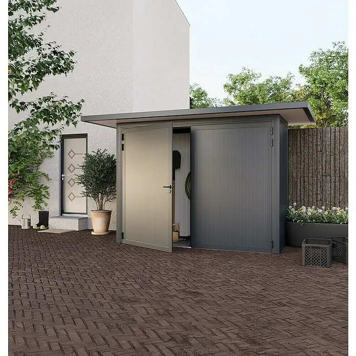 Wismar-NFI Gerätehaus Iris 31-2V - Außenbreite inkl. Dachüberstand: 425 cm, Außentiefe inkl. Dachüberstand: 225 cm, Stahl, Anthrazit/Weiß - Ein graues Gerätehaus mit leicht geöffneter Tür steht auf einer gepflasterten Fläche vor einem Haus.
