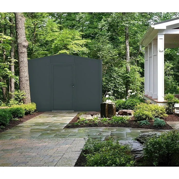 Wismar-NFI Gerätehaus Aster 1V - Außenmaß inkl. Dachüberstand (B x T): 325 x 125 cm, Stahl, Anthrazit/Weiß, Einzeltür - Ein graues Metall-Gartenschuppen steht auf einem gepflasterten Weg neben einem Haus. Ideal für die Gartenaufbewahrung und Geräte.