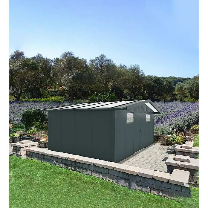 Wismar-NFI Gerätehaus Pisselint 64 - Außenmaß inkl. Dachüberstand (B x T): 685 x 485 cm, Stahl, Anthrazit/Weiß - Eine graue Metall-Gartenhütte mit Fenstern und Ziegeldach steht auf einem gepflasterten Bereich in einem Garten.